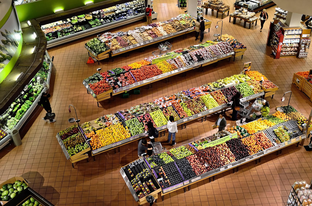 Mano di donna che scansiona il codice a barre di una confezione di verdure fresche al supermercato, smartphone con app di confronto prezzi sullo sfondo, scaffali con prodotti italiani