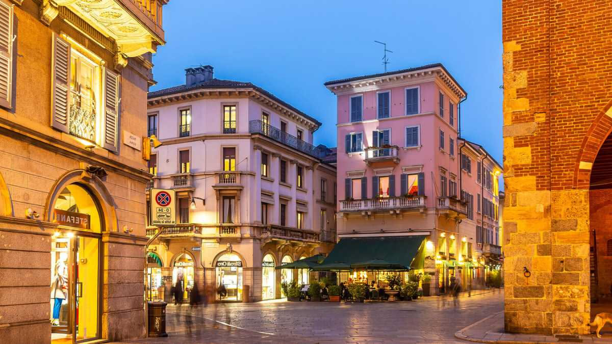 Interno di una caffetteria moderna a Verona con tavoli in legno, vista su piazza con architettura medievale sullo sfondo, clienti al bancone
