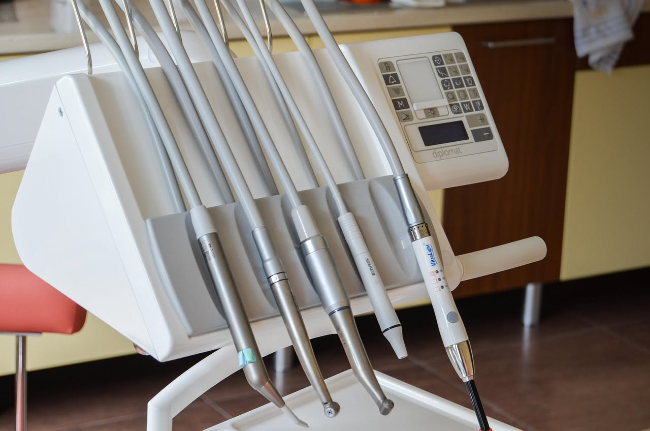 Studio dentistico con poltrona bianca, strumenti sterilizzati su vassoi in acciaio, assistente in camice celeste che aiuta il dentista durante una visita
