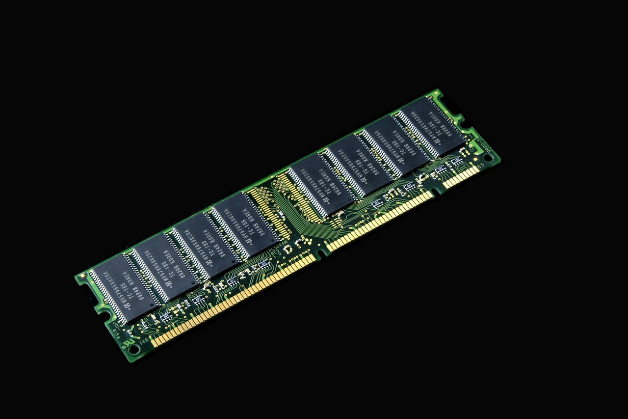Modulo di memoria RAM color oro inserito in uno slot di una scheda madre con componenti elettronici visibili, sfondo blu scuro