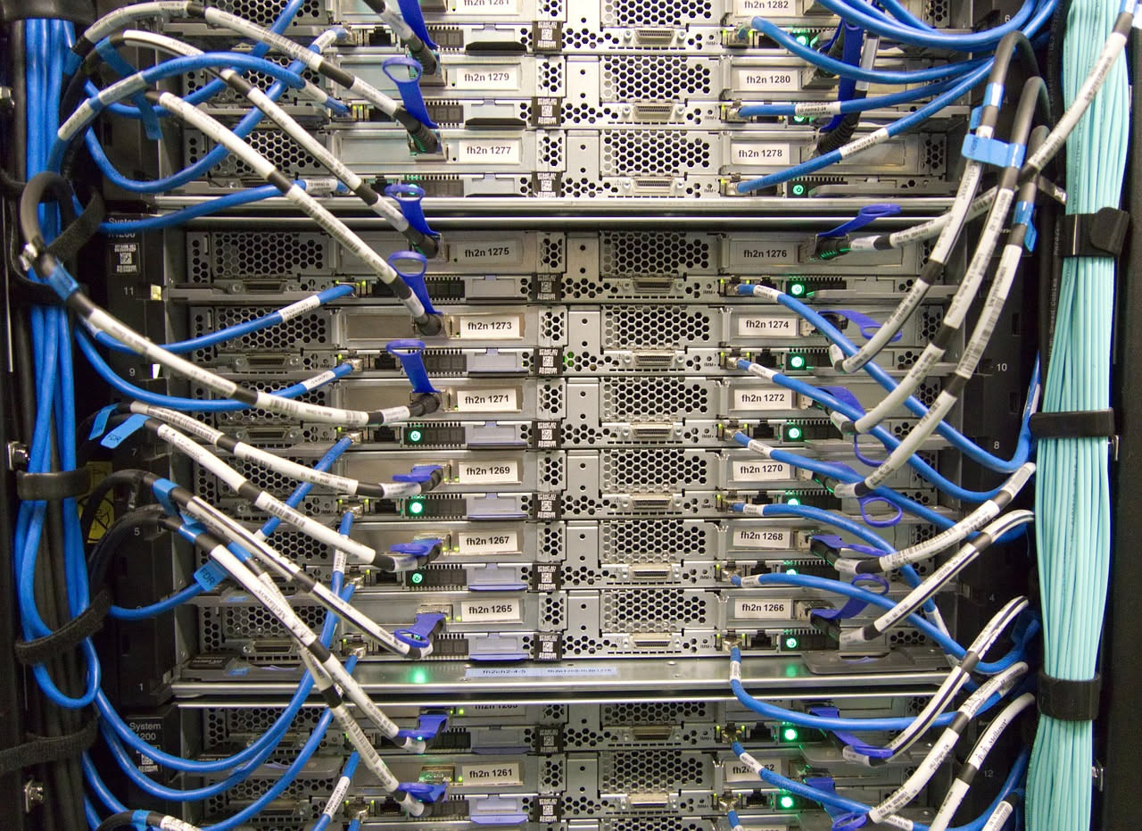 Stanza con armadi contenenti server illuminati, cavi di rete blu e rossi, spie luminose verdi e blu, sfondo grigio di data center