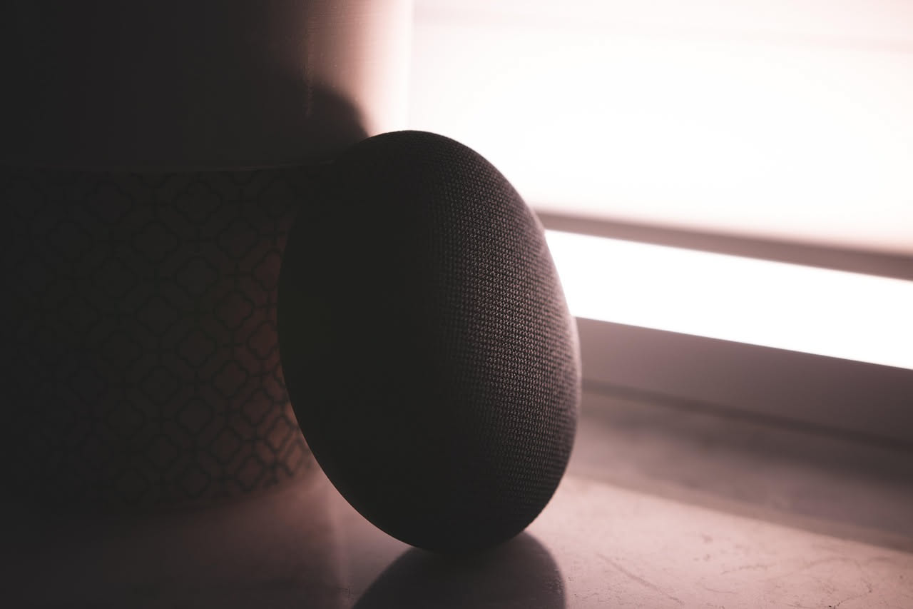Dispositivo smart speaker bianco con microfono integrato su una scrivania, anelli luminosi attorno alla parte superiore che si illuminano durante il riconoscimento vocale