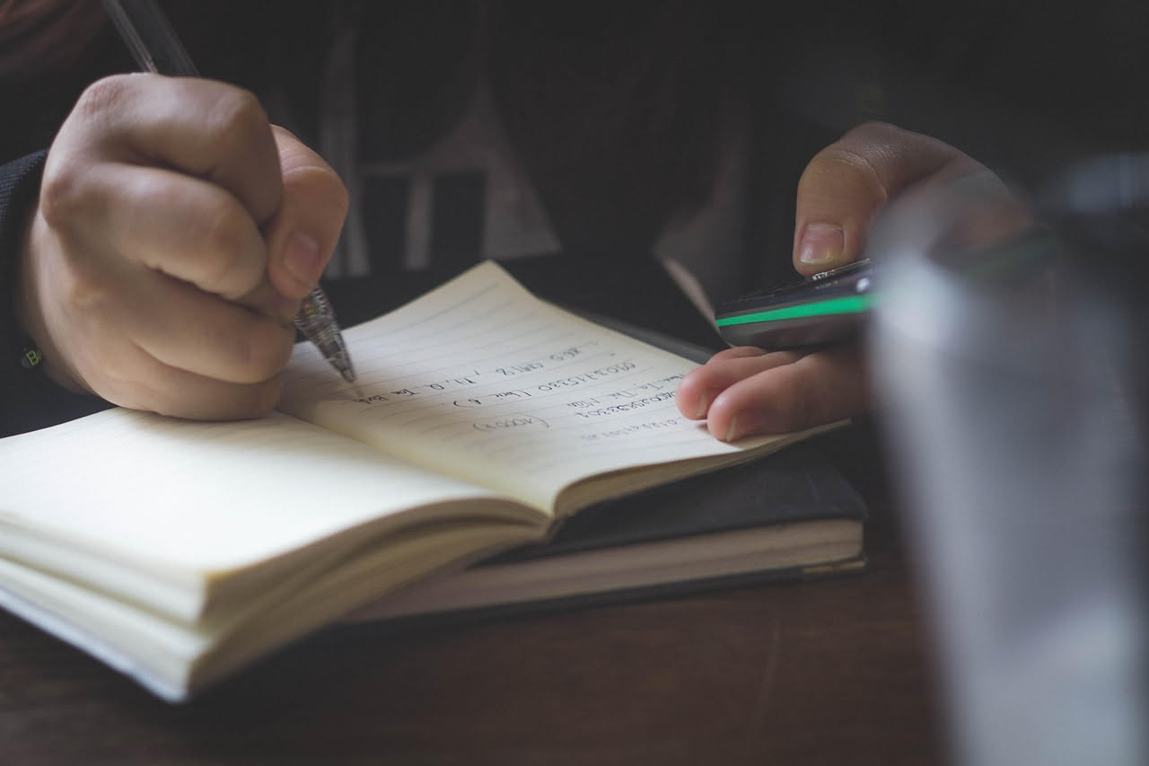 Persona che digita al computer con sullo schermo testo di ricerca e mappe concettuali, accanto a libri aperti e quaderno con appunti